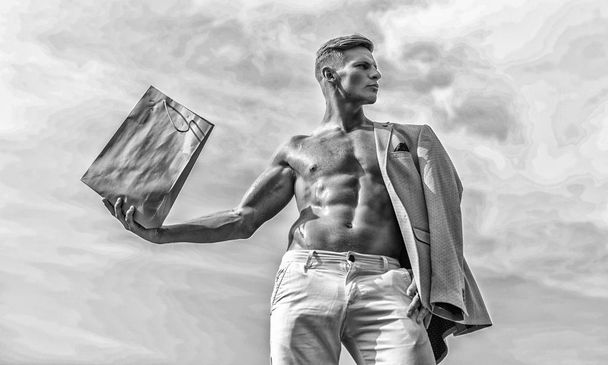 Man muscular athlete hold shopping bag sky background. Hot sales and discount. Guy attractive macho carry shopping bag made out of brown paper. Sales season. Take this package. Shop assistant concept - Fotoğraf, Görsel