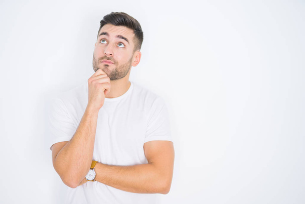 Young handsome man wearing casual white t-shirt over white isolated background with hand on chin thinking about question, pensive expression. Smiling with thoughtful face. Doubt concept. - Foto, Imagem