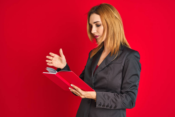 Jonge mooie roodharige zakenvrouw draagt pak leesboek - Foto, afbeelding