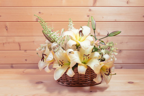 Wicker basket with beige colored lilies and white astilbe and hydrangea flowers on wooden table.  - Photo, Image