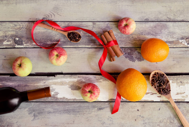 Mulled wine recipe ingredients. Bottle of red wine, oranges, cinnamon sticks, anise, cloves and apples on aged wooden background.  - Foto, afbeelding
