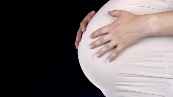Pregnant woman stroking her big belly with her hands. Woman in a light T-shirt - Imágenes, Vídeo