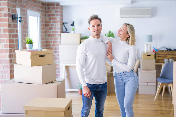 Young beautiful couple standing at new home around cardboard boxes - Photo, Image