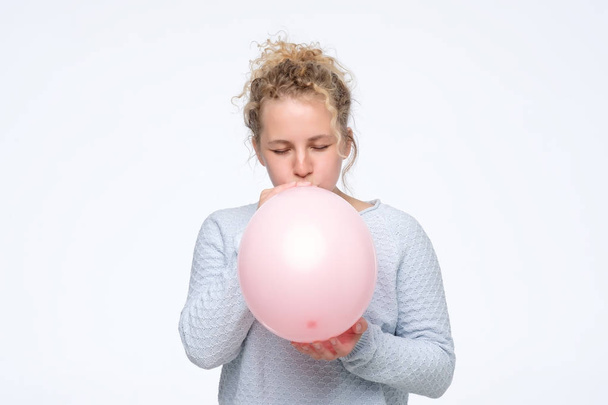 woman in gblue sweateris blowing pink balloon preparing for birthday party - Foto, afbeelding