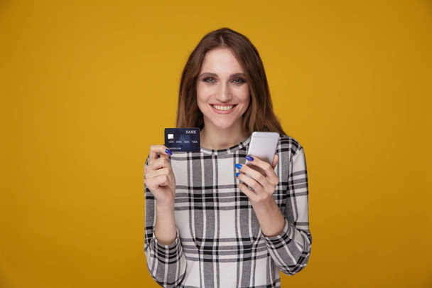 Красивая женщина показывает кредитную карту и с помощью мобильного телефона стоять изолированы
. - Фото, изображение
