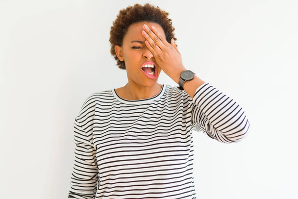 Mladá krásná africká Američanka nosí pruhy svetr na bílém pozadí Zívání unavený pokrývající polovinu obličeje, oko a ústa s rukou. Tvář bolí bolestí. - Fotografie, Obrázek