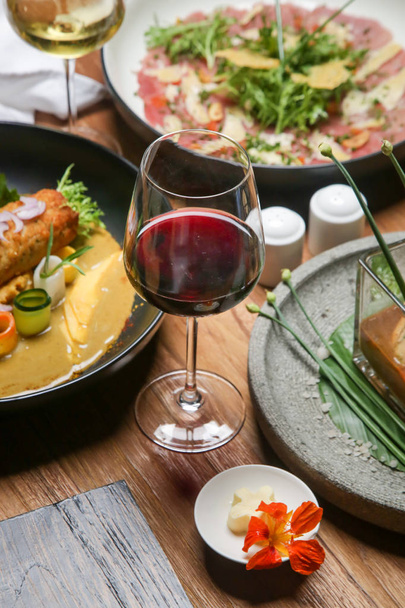 Όμορφα διακοσμημένα γεύματα και ποτήρια λευκού και κόκκινου κρασιού στο ξύλινο τραπέζι - Φωτογραφία, εικόνα