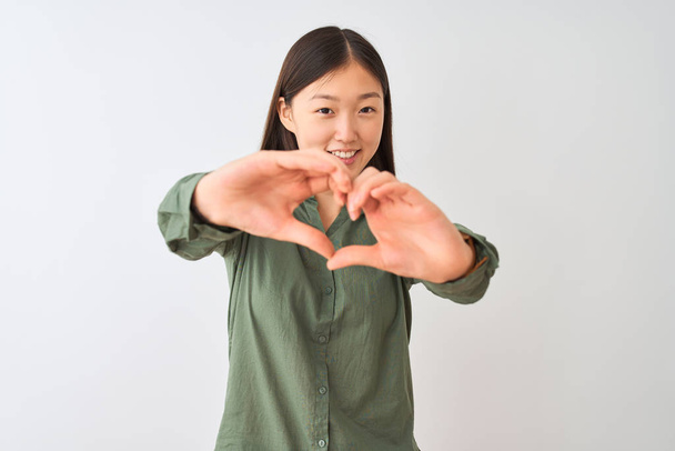 Giovane donna cinese indossa casual camicia verde in piedi sopra isolato sfondo bianco sorridente in amore mostrando il simbolo del cuore e la forma con le mani. Concetto romantico
. - Foto, immagini