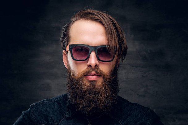 Hombre barbudo atractivo en gafas de sol sobre fondo oscuro
. - Foto, imagen