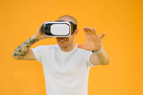 Мальчик играет на VR очках в помещении и веселится с наушниками. Прикосновение воздуха во время виртуальной реальности на оранжевом фоне
 - Фото, изображение