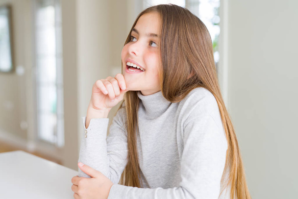 美しい少女の子供の質問について考える顎の手でタートルネックセーターを着て、集中的な表現。思慮深い顔で微笑んだ。疑いの概念. - 写真・画像