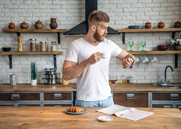 It's time to go to work. Handsome bearded man looking at his watch and realizing that he is late for work or study at his breakfast. - Foto, imagen
