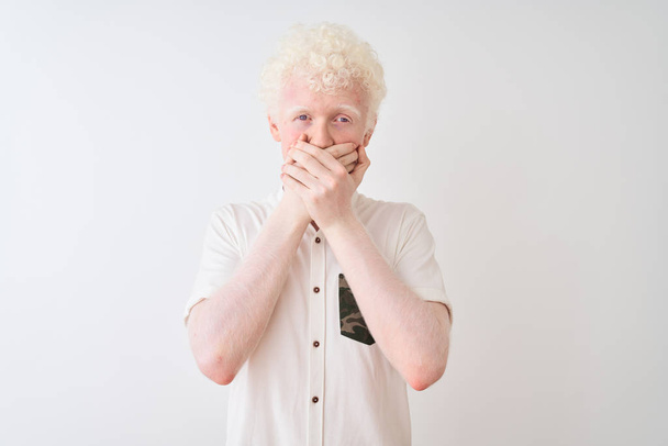 Nuori albiino vaalea mies päällään rento paita seisoo yli eristetty valkoinen tausta järkyttynyt peittää suu kädet erehdyksen. Salainen käsite
. - Valokuva, kuva