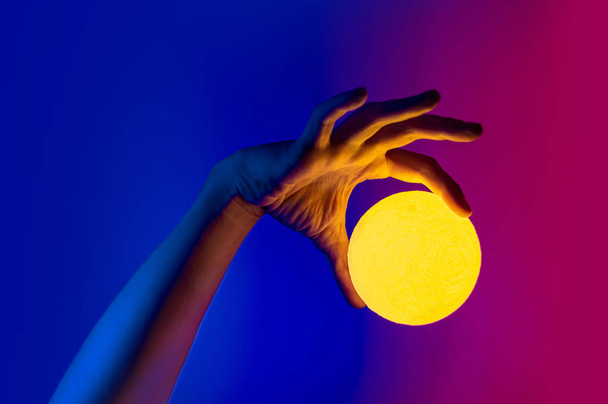 Hombre sosteniendo la forma de luna amarilla esfera iluminada. Estilo surrealista de la foto, elemento de arte contemporáneo para el diseño, carteles y pancartas. Luz azul neón y púrpura
. - Foto, imagen