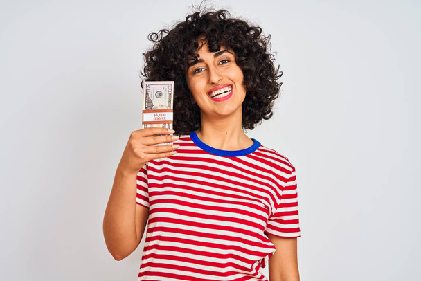 Young arab woman with curly hair holding dollars standing over isolated white background with a happy face standing and smiling with a confident smile showing teeth - Photo, Image