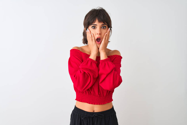 Young beautiful woman wearing red summer t-shirt standing over isolated white background afraid and shocked, surprise and amazed expression with hands on face - Foto, immagini