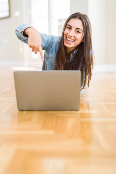 Bella giovane donna sdraiata sul pavimento con il computer portatile molto felice che punta con mano e dito
 - Foto, immagini