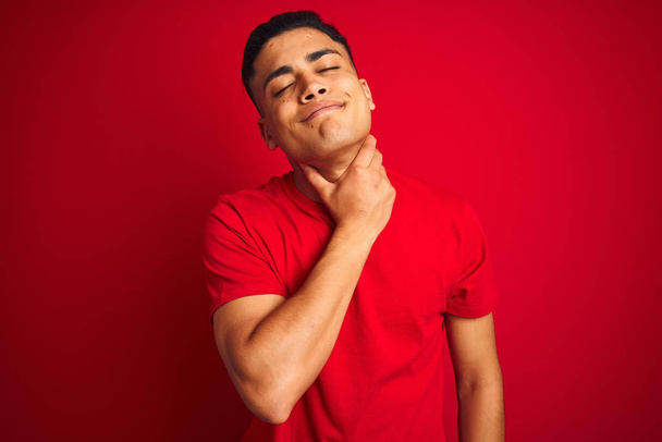 Jovem brasileiro vestindo camiseta em pé sobre fundo vermelho isolado Tocando no pescoço doloroso, dor de garganta por gripe, cravo e infecção
 - Foto, Imagem
