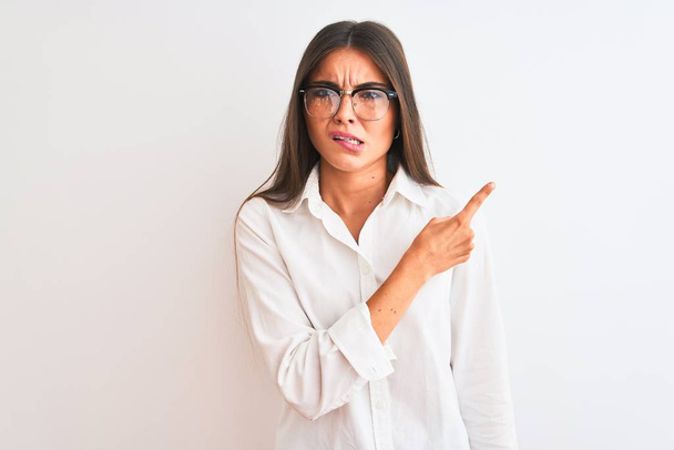 Young beautiful businesswoman wearing glasses standing over isolated white background Pointing aside worried and nervous with forefinger, concerned and surprised expression - Foto, immagini