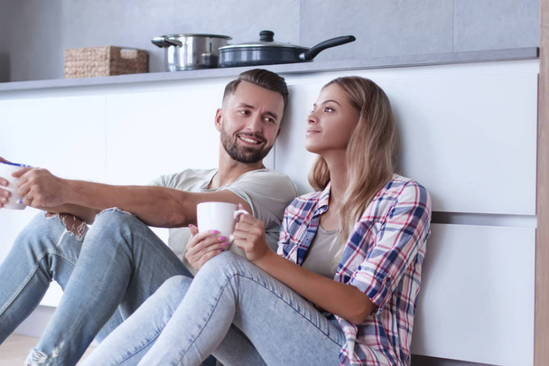 young couple drinking coffee sitting on the kitchen floor - 写真・画像