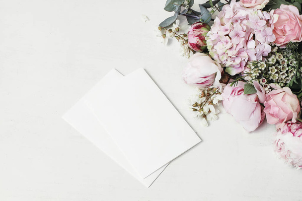 Feminine wedding, birthday mock-up scene. Decorative floral corner of peony, hydrangea, roses and locust flowers. Blank paper greeting cards on white wooden table background. Fat lay, top view - Foto, Imagen
