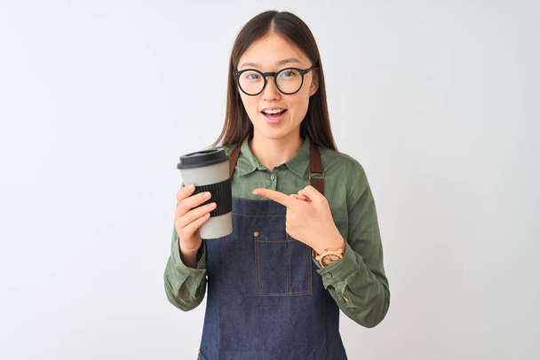 Barista chinois femme portant tablier verres boire du café sur fond blanc isolé très heureux pointage avec la main et le doigt
 - Photo, image