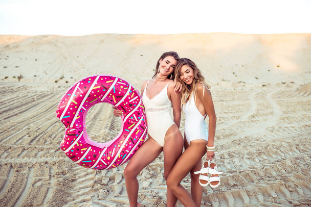 Two girls girlfriends, happy, smiling, laughing and playing, summer jacket, playing tan with an inflatable toy cheesecake circle donut. Emotions of holiday fun, birthday in summer on curt. - Foto, Imagem