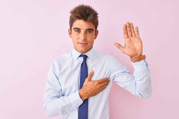Nuori komea liikemies yllään paita ja solmio seisoo yli eristetty vaaleanpunainen tausta vannoo käsi rinnassa ja avoin kämmen, jolloin uskollisuus lupaus vala
 - Valokuva, kuva