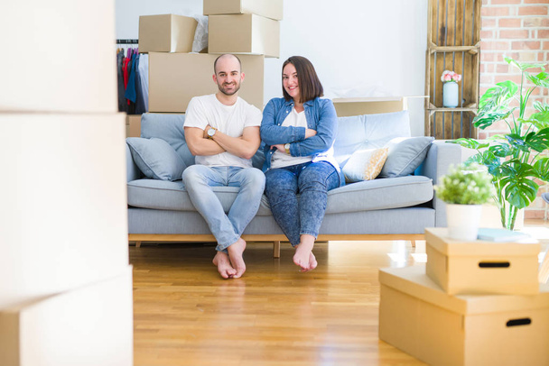 Young couple sitting on the sofa arround cardboard boxes moving to a new house happy face smiling with crossed arms looking at the camera. Positive person. - 写真・画像
