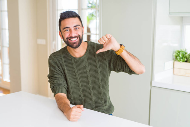 Красивый латиноамериканец в обычном свитере дома выглядит уверенно с улыбкой на лице, указывая на себя пальцами гордым и счастливым
. - Фото, изображение
