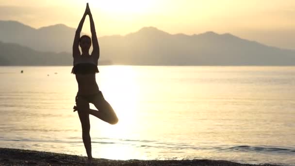 4k-A kecses lány csinál jóga jelent a tengerparton napkelte, lassított - Felvétel, videó