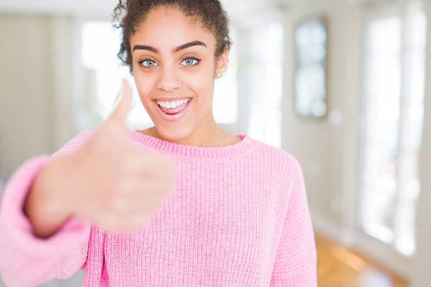 Beautiful young african american woman with afro hair doing happy thumbs up gesture with hand. Approving expression looking at the camera showing success. - Photo, Image