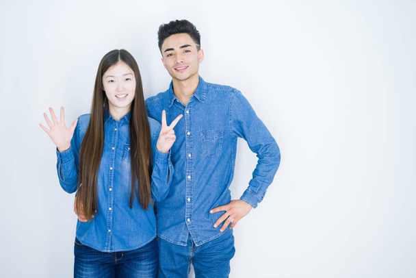 Hermosa joven asiática pareja sobre blanco aislado fondo mostrando y apuntando hacia arriba con los dedos número siete mientras sonríe confiado y feliz
. - Foto, Imagen