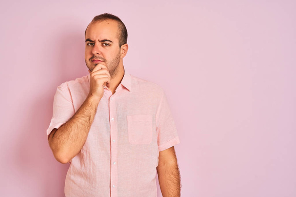 Молодий чоловік в елегантній сорочці стоїть над ізольованим рожевим тлом, впевнено дивиться на камеру з посмішкою з схрещеними руками і піднятою рукою на підборідді. Мислення позитивне
. - Фото, зображення