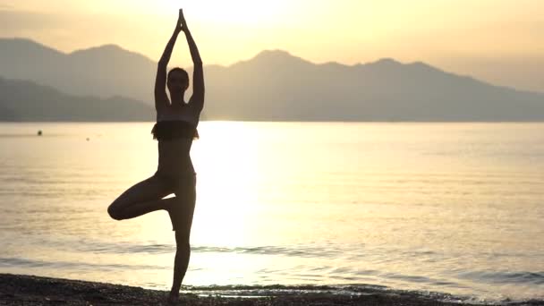 4k - female silhouette doing yoga asana on the seashore at sunrise, slow motion - Footage, Video