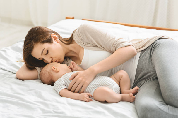 Jeune mère embrassant son nouveau-né endormi au lit
. - Photo, image