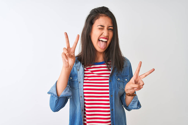 Jeune femme chinoise portant t-shirt rayé et chemise en denim sur fond blanc isolé souriant avec la langue montrant les doigts des deux mains faisant signe de victoire. Numéro deux
. - Photo, image