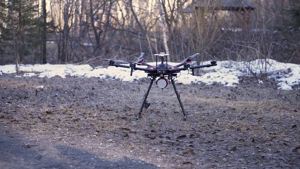 Un helicóptero con engranajes de aterrizaje volando hacia el suelo en el fondo del bosque de finales de otoño. Clip. Pequeño dron negro con cuchillas giratorias que aterriza en el suelo
. - Foto, imagen