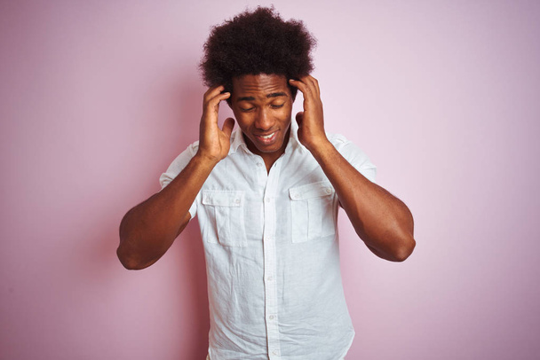 junger amerikanischer Mann mit Afro-Haaren trägt weißes Hemd, das über isoliertem rosa Hintergrund steht, mit der Hand auf dem Kopf vor Kopfschmerzen wegen Stress. Migräne. - Foto, Bild
