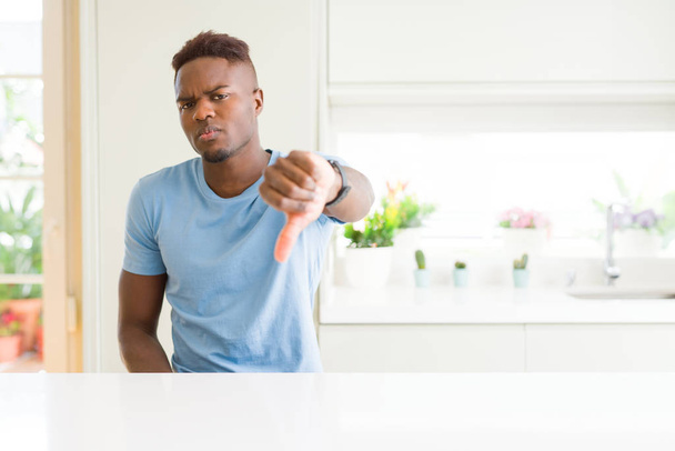 家庭でカジュアルなTシャツを着ているハンサムなアフリカ系アメリカ人の男性は、親指を下にジェスチャーで拒絶と否定を示して不満と怒っているように見えます。悪い表現. - 写真・画像