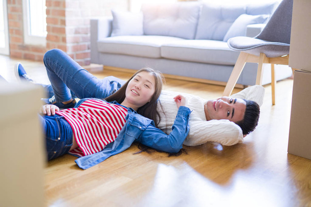 Young asian couple lying on the floor of new house arround cardboard boxes relaxing and smiling happy - Photo, Image