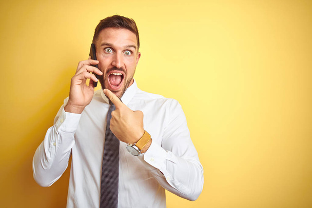 Young handsome business man talking on the phone over yellow isolated background very happy pointing with hand and finger - Foto, Imagem