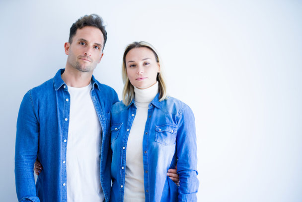 Молодая красивая пара в джинсовой рубашке, стоящая на изолированном белом фоне с серьезным выражением лица. Простой и естественный взгляд на камеру
. - Фото, изображение