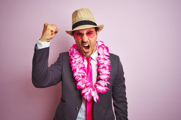 Молодой бизнесмен в костюме шляпа очки Гавайский лей на изолированном розовом фоне раздражен и разочарован кричать от гнева, сумасшедший и кричать с поднятой рукой, гнев концепции
 - Фото, изображение