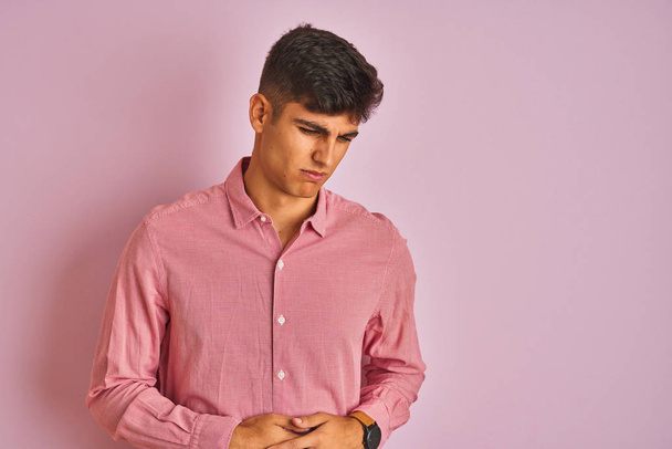 Молодий індійський чоловік у витонченій сорочці стоїть над ізольованим рожевим тлом з рукою на животі, тому що нудота, хвороба болюча почуваються погано. Концепція Ache
. - Фото, зображення