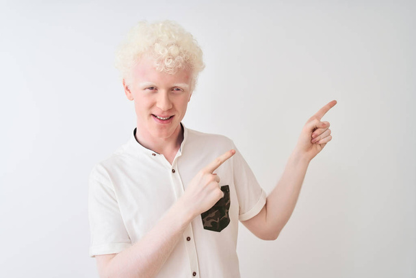 Jonge albino blonde man draagt casual shirt staan over geïsoleerde witte achtergrond glimlachen en kijken naar de camera wijzen met twee handen en vingers naar de zijkant. - Foto, afbeelding