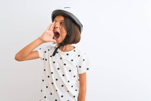 Krásné dítě dívka v helmě bezpečnostní kolo stojí nad izolované bílé pozadí křičí a křičí hlasitě na stranu s rukou na ústech. Koncept komunikace. - Fotografie, Obrázek