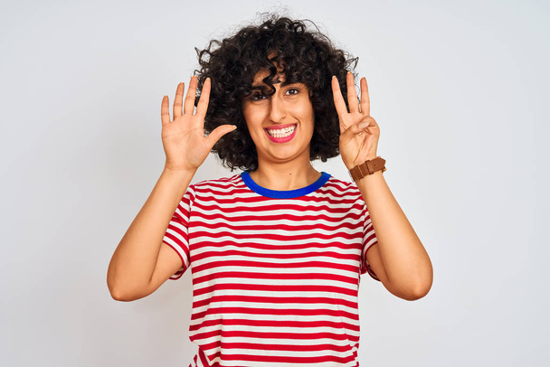 Young arab woman with curly hair wearing striped t-shirt over isolated white background showing and pointing up with fingers number eight while smiling confident and happy. - Fotoğraf, Görsel