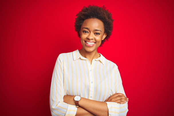 Joven mujer afroamericana hermosa con pelo afro sobre fondo rojo aislado cara feliz sonriendo con los brazos cruzados mirando a la cámara. Persona positiva
. - Foto, Imagen