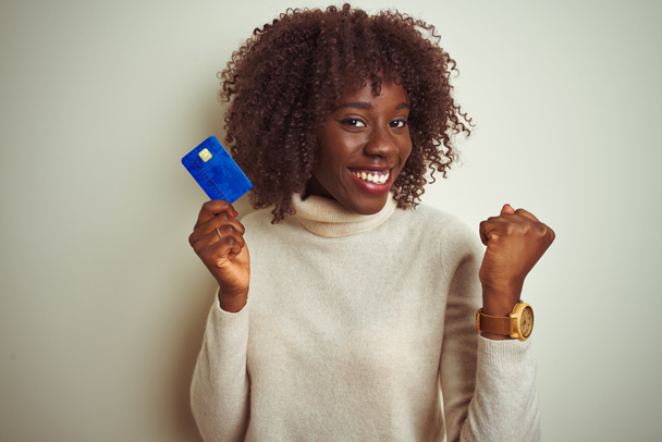 Giovane afro donna africana in possesso di carta di credito in piedi sopra isolato sfondo bianco urlando orgoglioso e celebrando la vittoria e il successo molto eccitato, emozione tifo
 - Foto, immagini